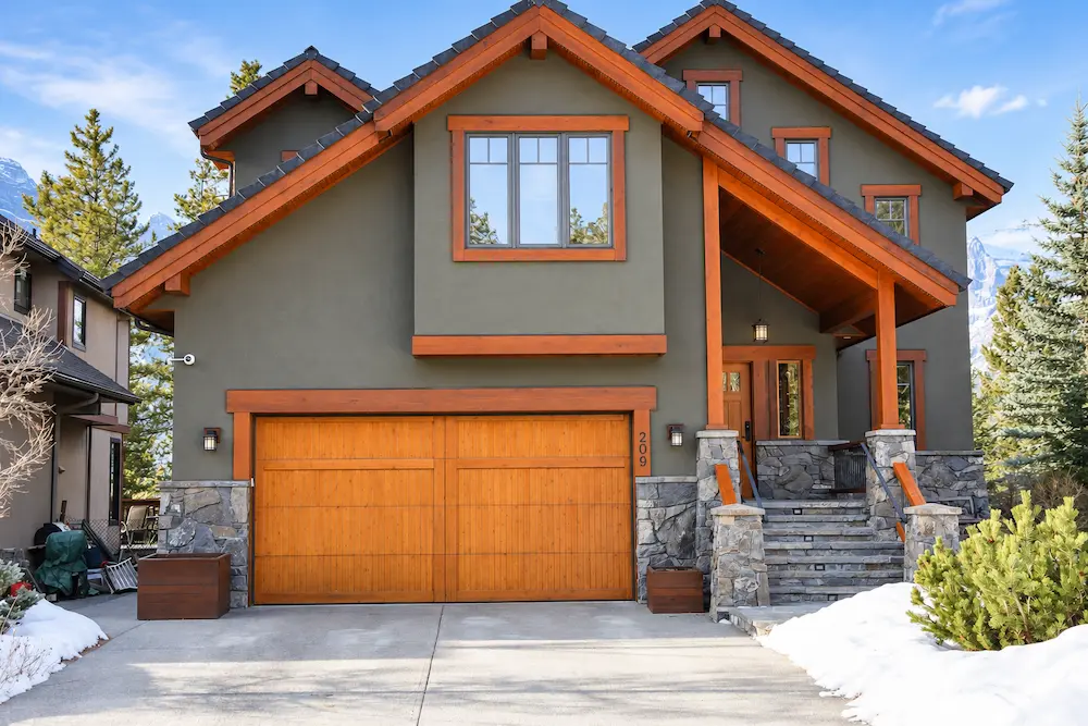 Grey two-storey house with natural wood trim, wood garage doors and stone accents.
